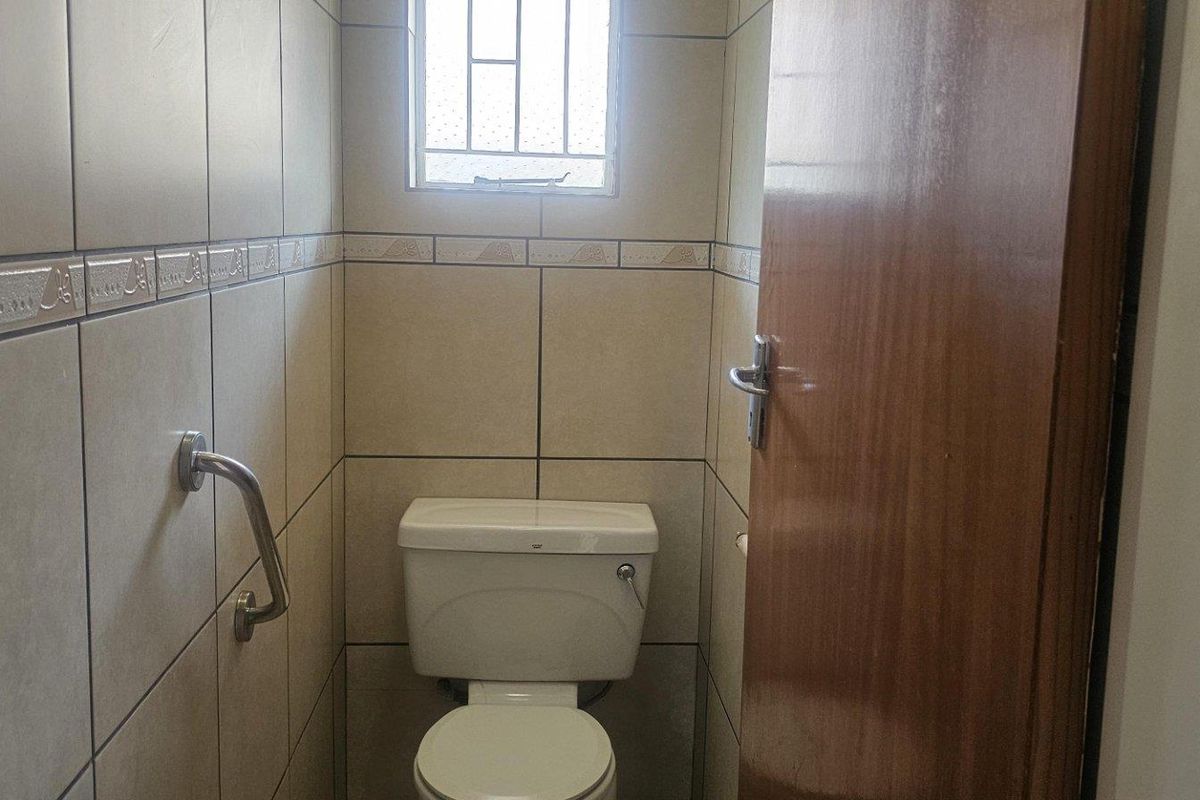 A compact guest toilet featuring floor-to-ceiling ceramic tiling, a standard white toilet suite, and a wall-mounted safety grab rail.