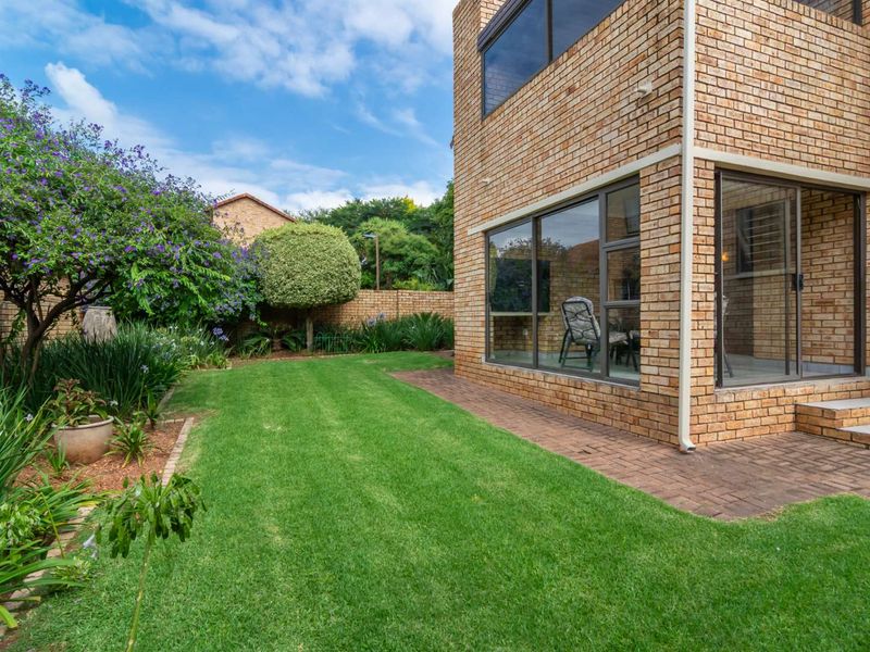 A well-maintained rear garden featuring a paved patio area, face brick exterior, and established landscaping.