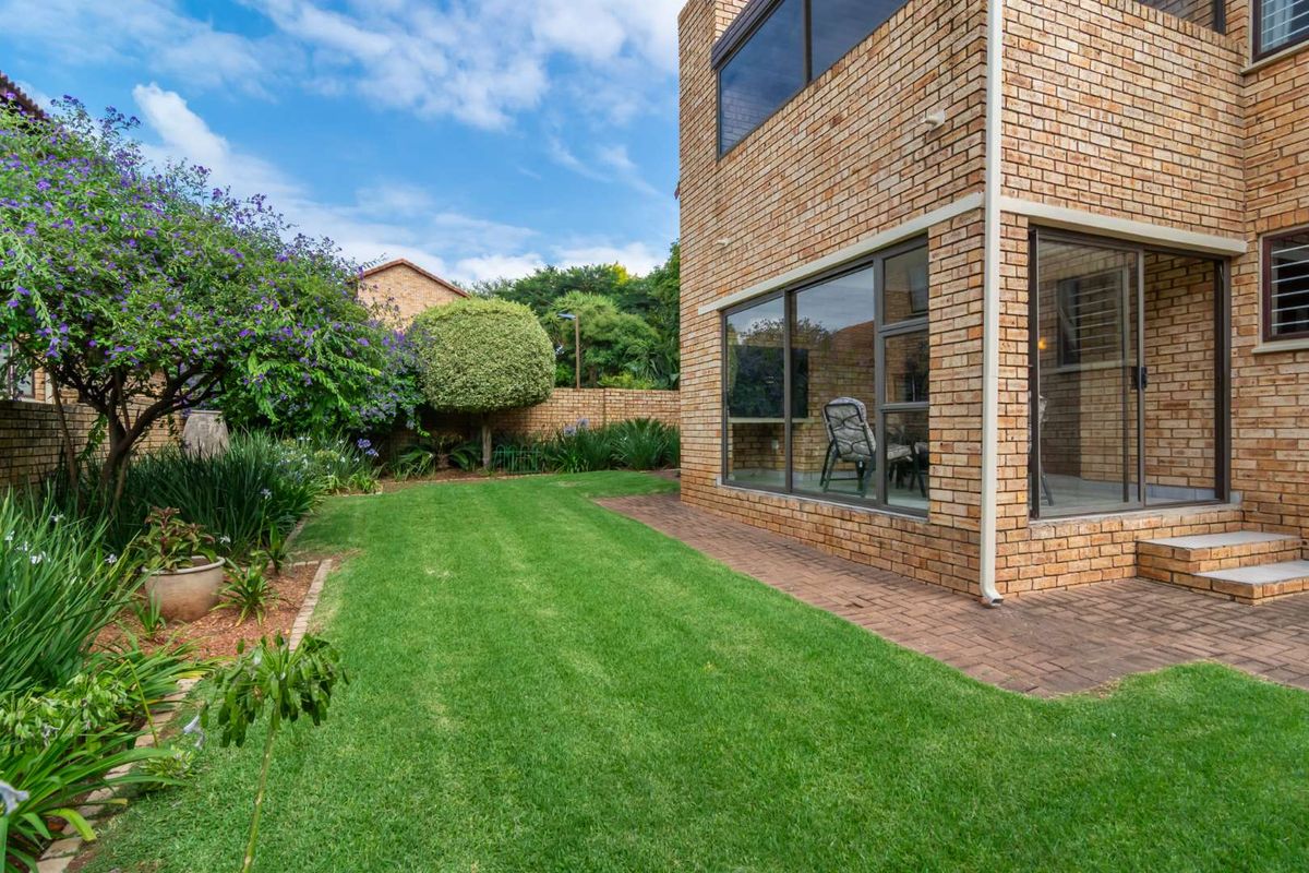 A well-maintained rear garden featuring a paved patio area, face brick exterior, and established landscaping.