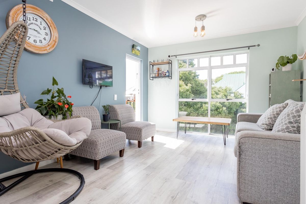 A bright and well-maintained living room featuring light-toned laminate flooring, a large glass sliding door providing natural light, and modern blue accent wall.