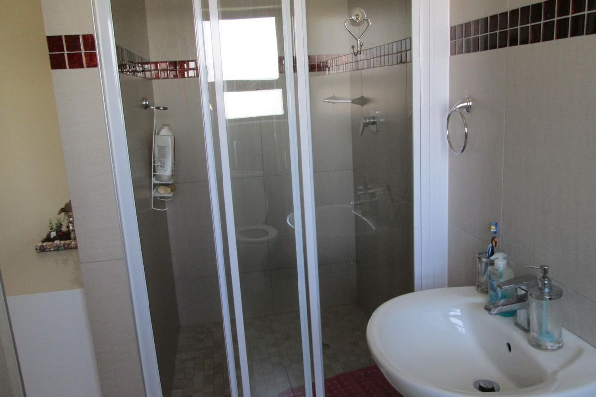 A functional bathroom featuring a glass-enclosed shower, a pedestal basin, and tiled walls with a decorative mosaic border.