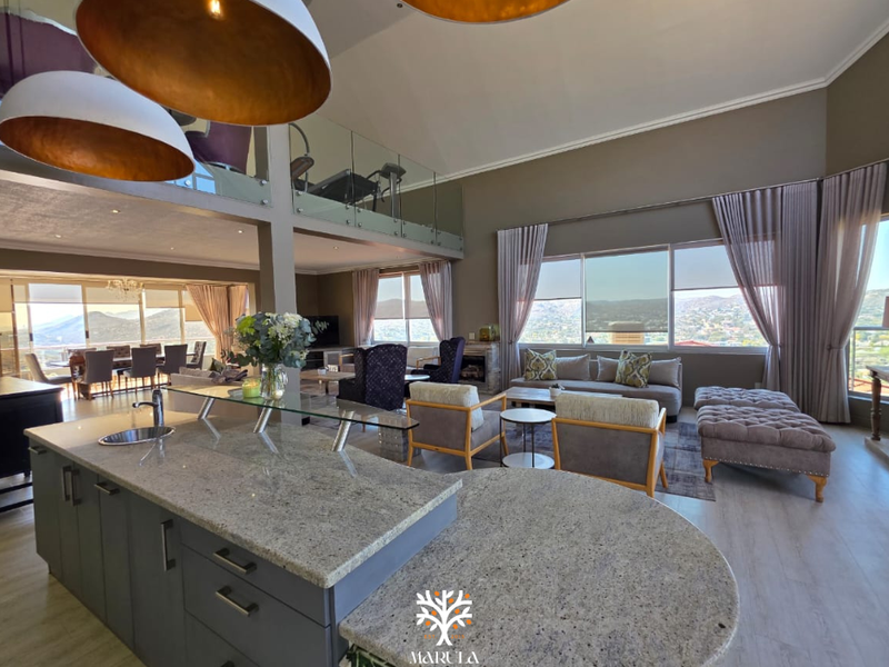 Spacious open-plan living area featuring a large granite kitchen island, vaulted ceilings, and a mezzanine level with glass balustrades overlooking the main space.
