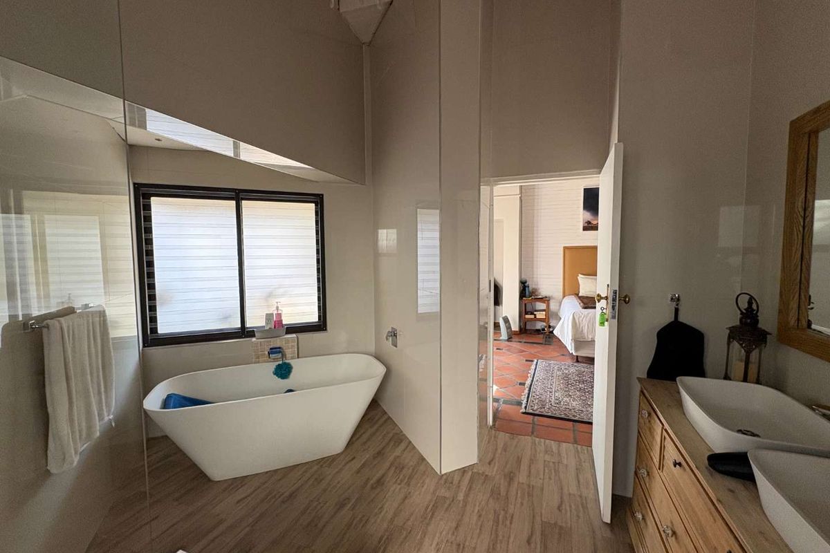 A modern bathroom featuring a freestanding bathtub, dual vessel sinks on a wooden vanity, and a glass-enclosed shower area.