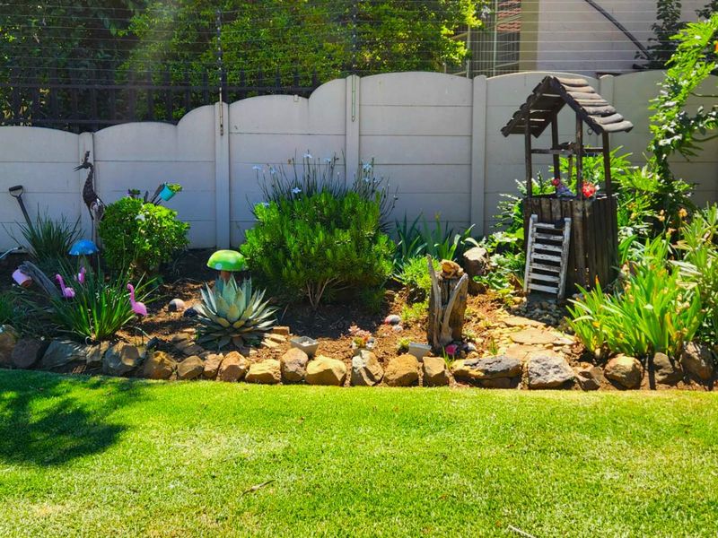A well-maintained garden area featuring a manicured lawn, stone-edged flower beds, and a secure precast concrete boundary wall with electric fencing.