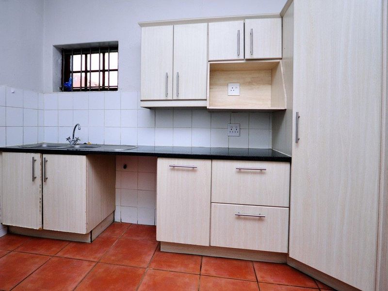 A functional kitchen featuring light-toned laminate cabinetry, granite countertops, a stainless steel sink, and terracotta floor tiles with a tiled backsplash.