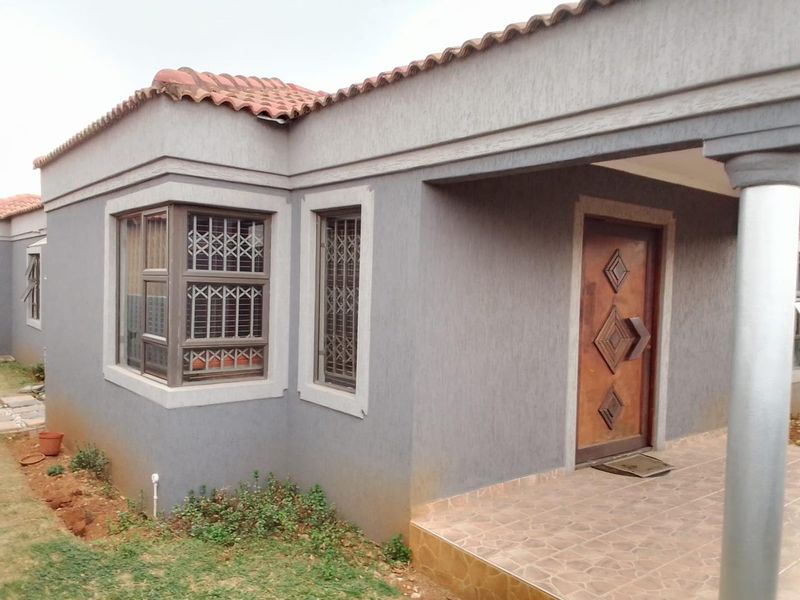 Front entrance view of a house featuring a tiled porch, decorative wooden door, and textured grey exterior walls with security-fitted windows.
