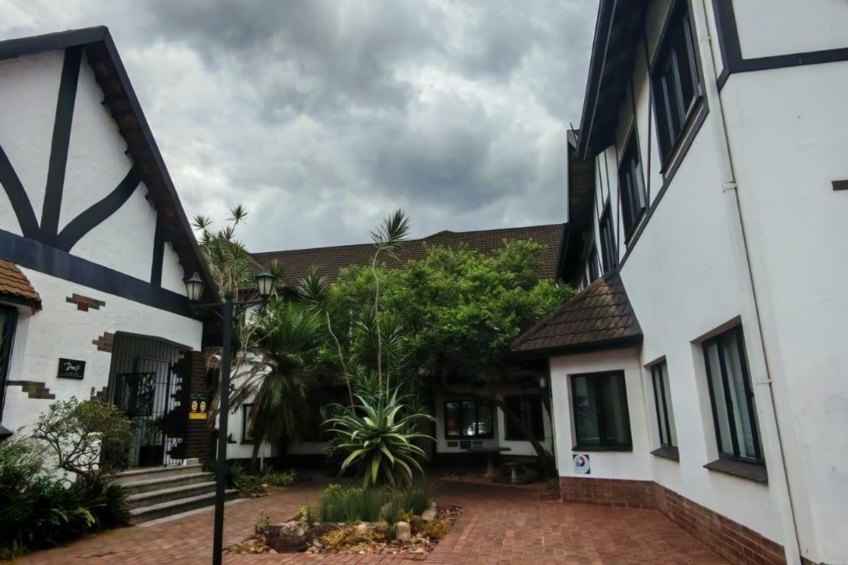 A charming courtyard area featuring Tudor-style architecture with timber framing, brick paving, and mature landscaping between two building wings.