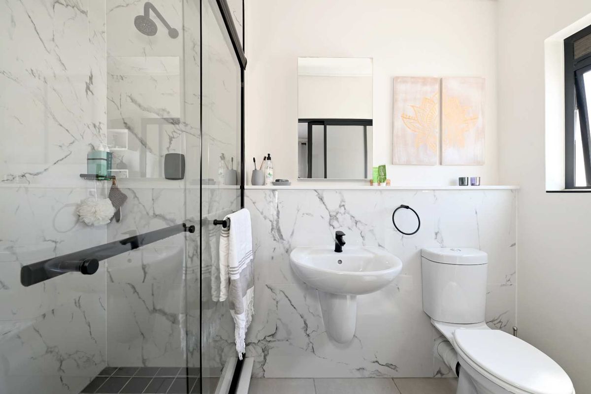 Modern bathroom featuring marble-look wall tiles, a glass shower enclosure, a pedestal sink with black fixtures, and a clean, contemporary design.