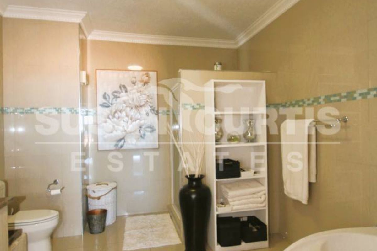 A spacious bathroom featuring a corner soaking tub, a separate glass-enclosed shower, and neutral wall tiling.