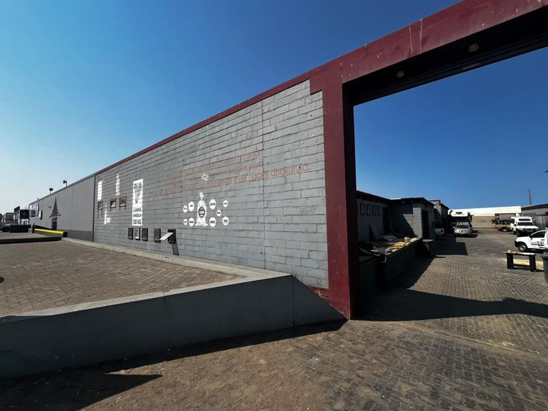 Exterior view of an industrial property featuring a large concrete block wall, paved driveway, and steel structural framing.