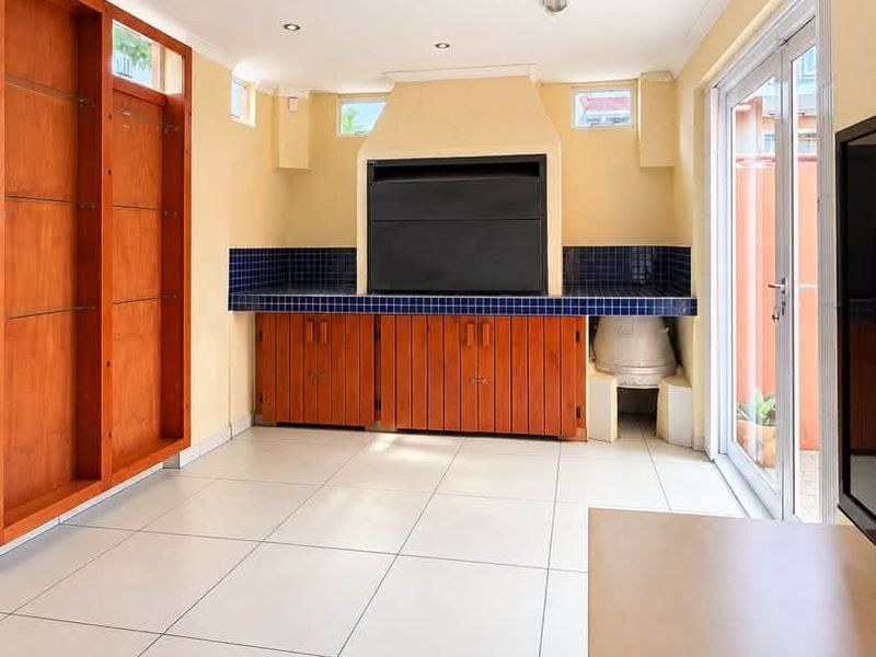 An enclosed patio area featuring a built-in braai, tiled flooring, and ample built-in wooden cabinetry, providing a functional space for indoor-outdoor entertaining.