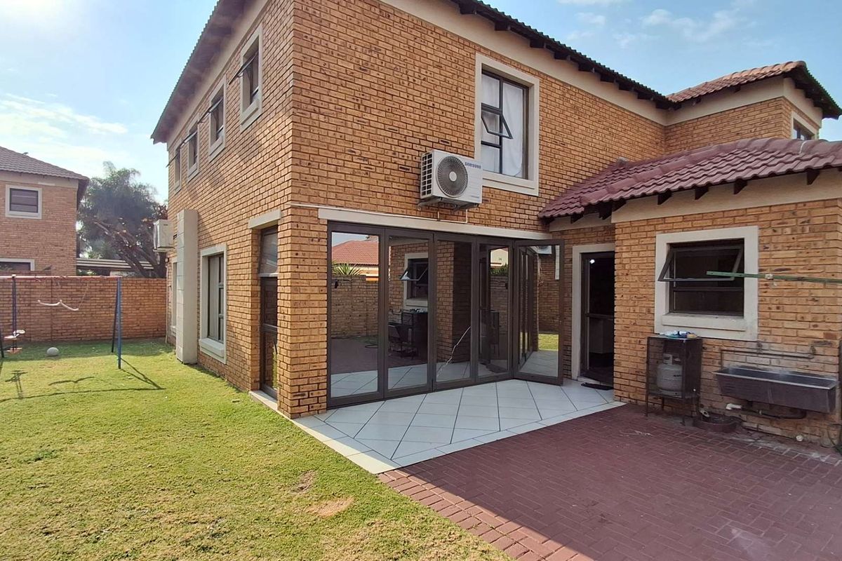 Rear view of a double-storey face brick house featuring a tiled patio with aluminium stacker doors, paved outdoor space, and a private garden.