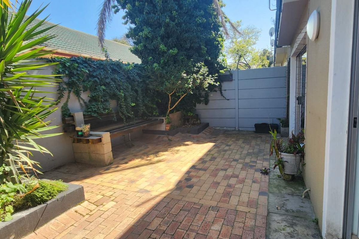 A private rear courtyard featuring brick paving, a built-in bench, and established garden borders, accessible via a sliding door from the main living area.