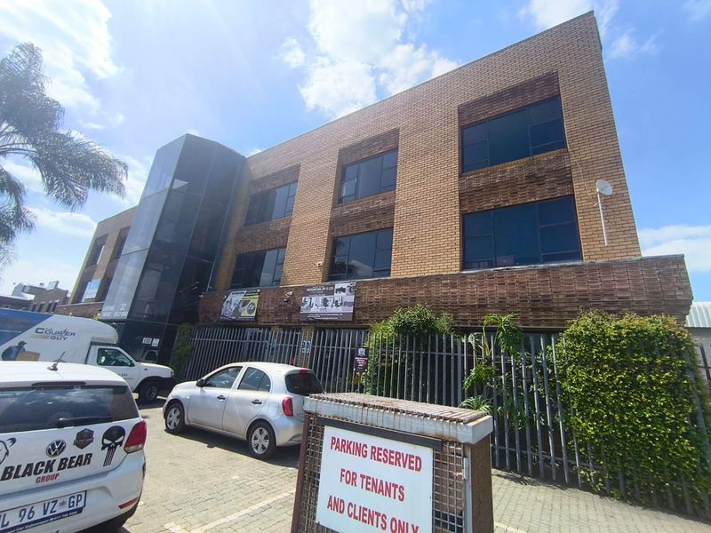 A multi-story commercial office building featuring a brick facade, glass elevator shaft, and dedicated paved parking area for tenants and clients.