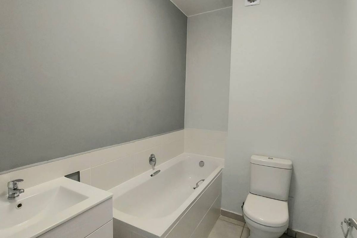 A clean, modern bathroom featuring a built-in bathtub, a vanity basin with storage, and a standard toilet.