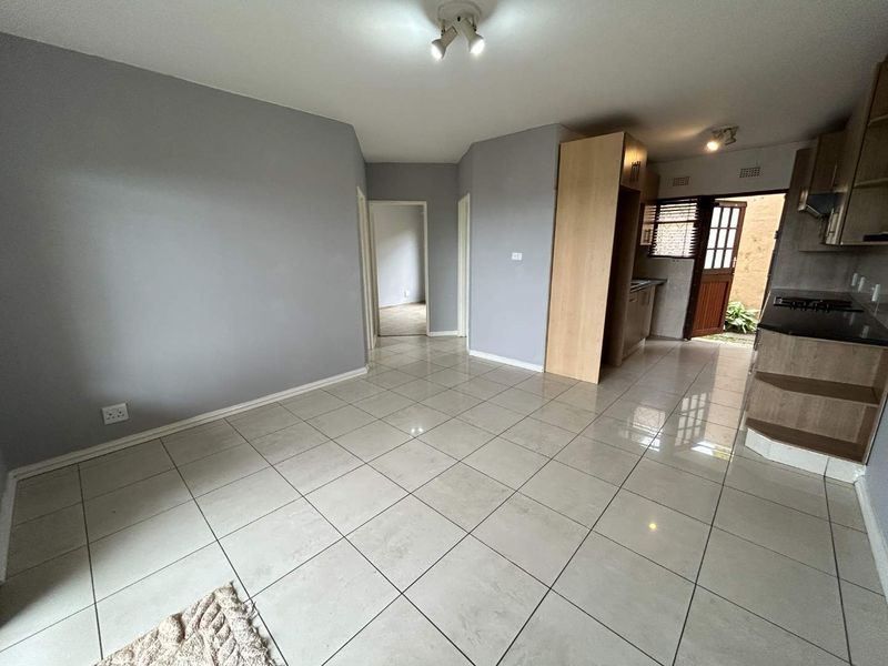 An open-plan living and kitchen area featuring neutral grey walls, polished floor tiles, and built-in kitchen cabinetry with a hob and extractor fan.