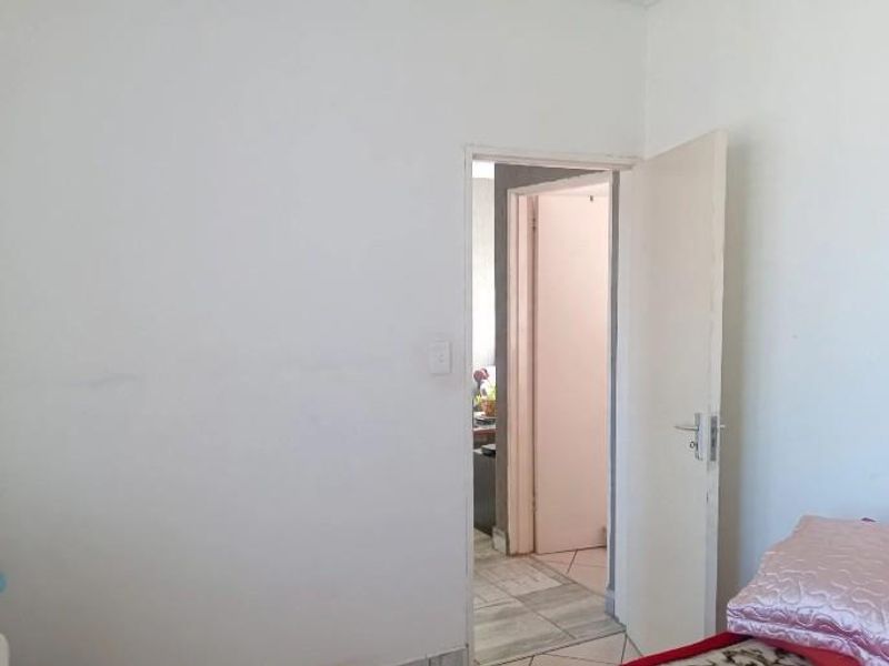 A simple bedroom interior featuring a plain white wall and an open doorway leading to an adjacent hallway.