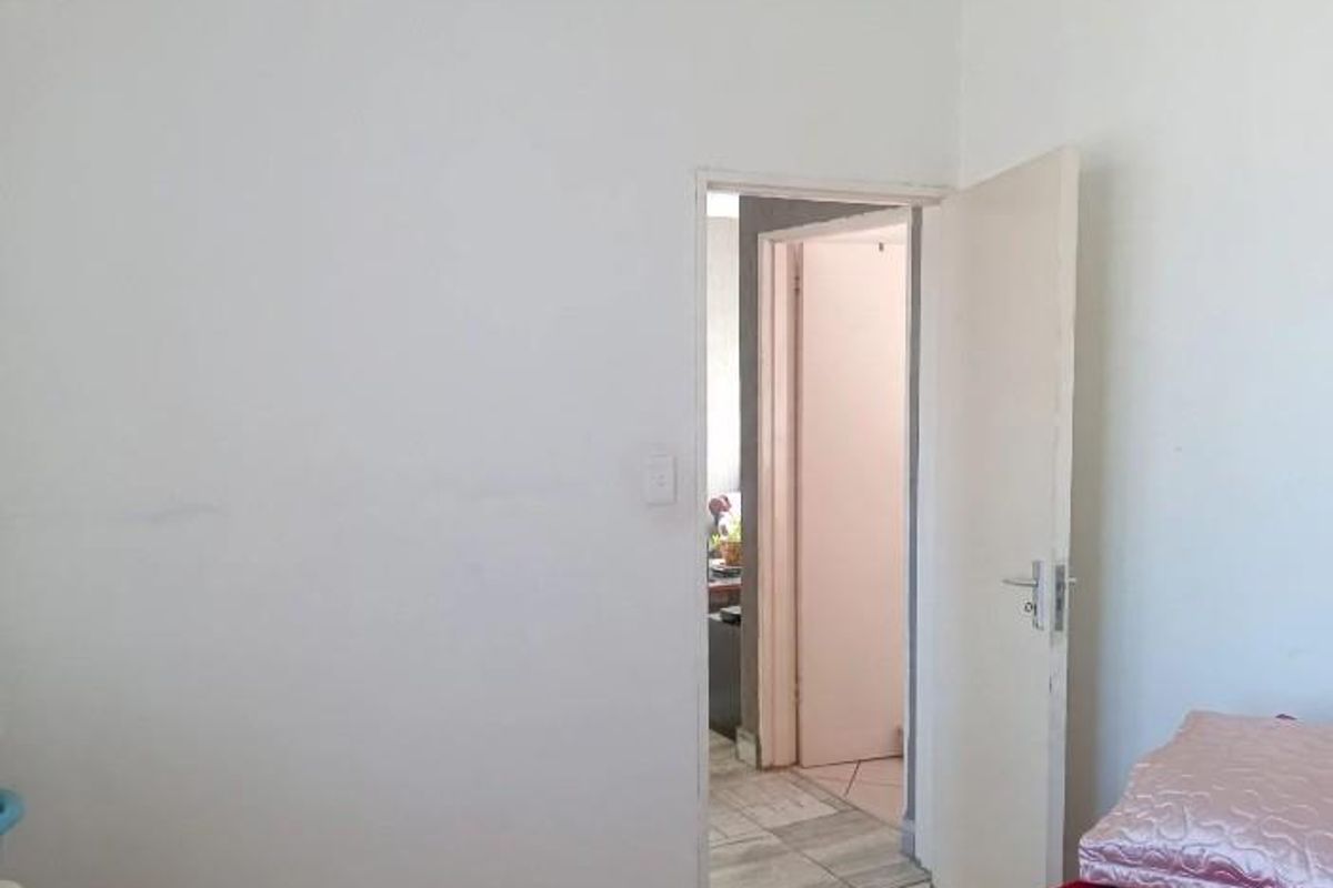 A simple bedroom interior featuring a plain white wall and an open doorway leading to an adjacent hallway.