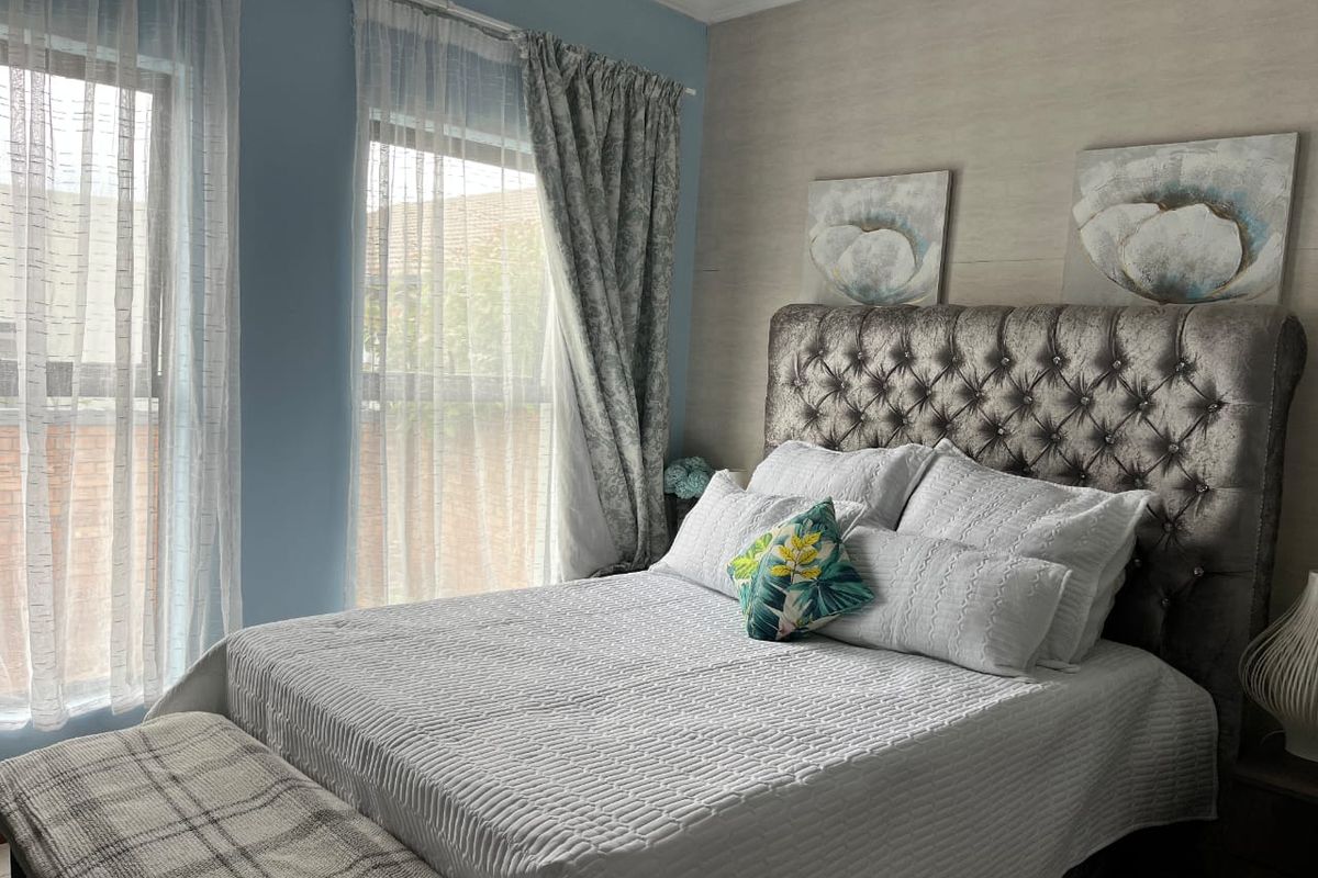 A well-lit bedroom featuring large windows with natural light, neutral wall finishes, and crown molding detail.
