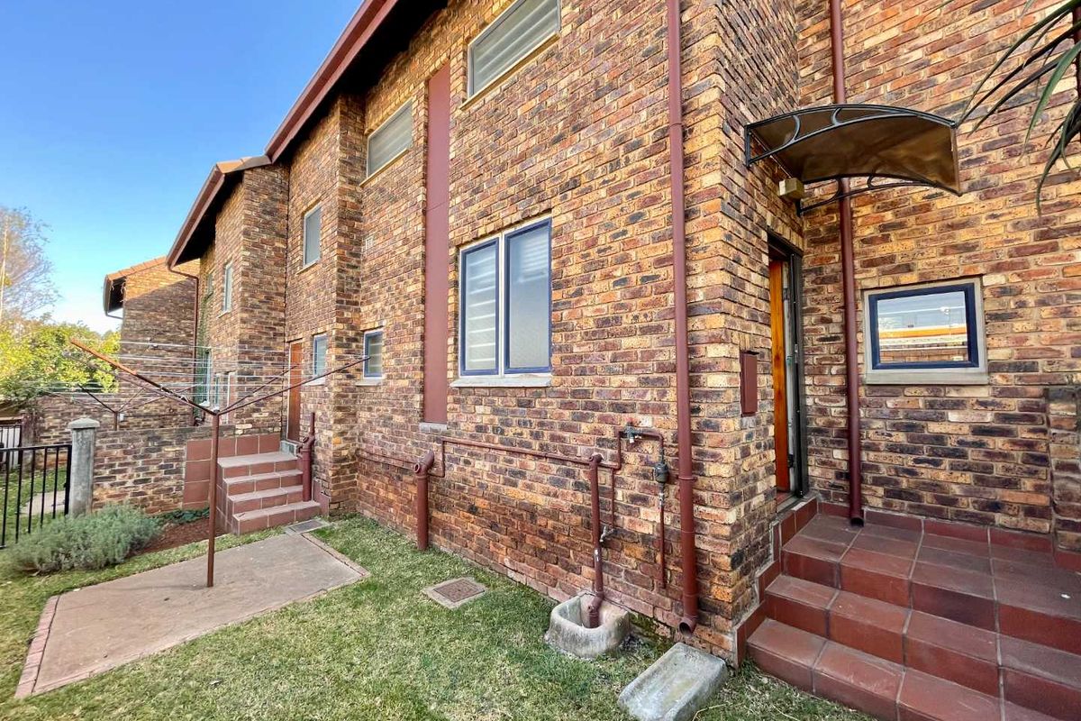 Rear exterior view of the townhouse featuring face brick construction, tiled entrance steps, and a small concrete patio area.