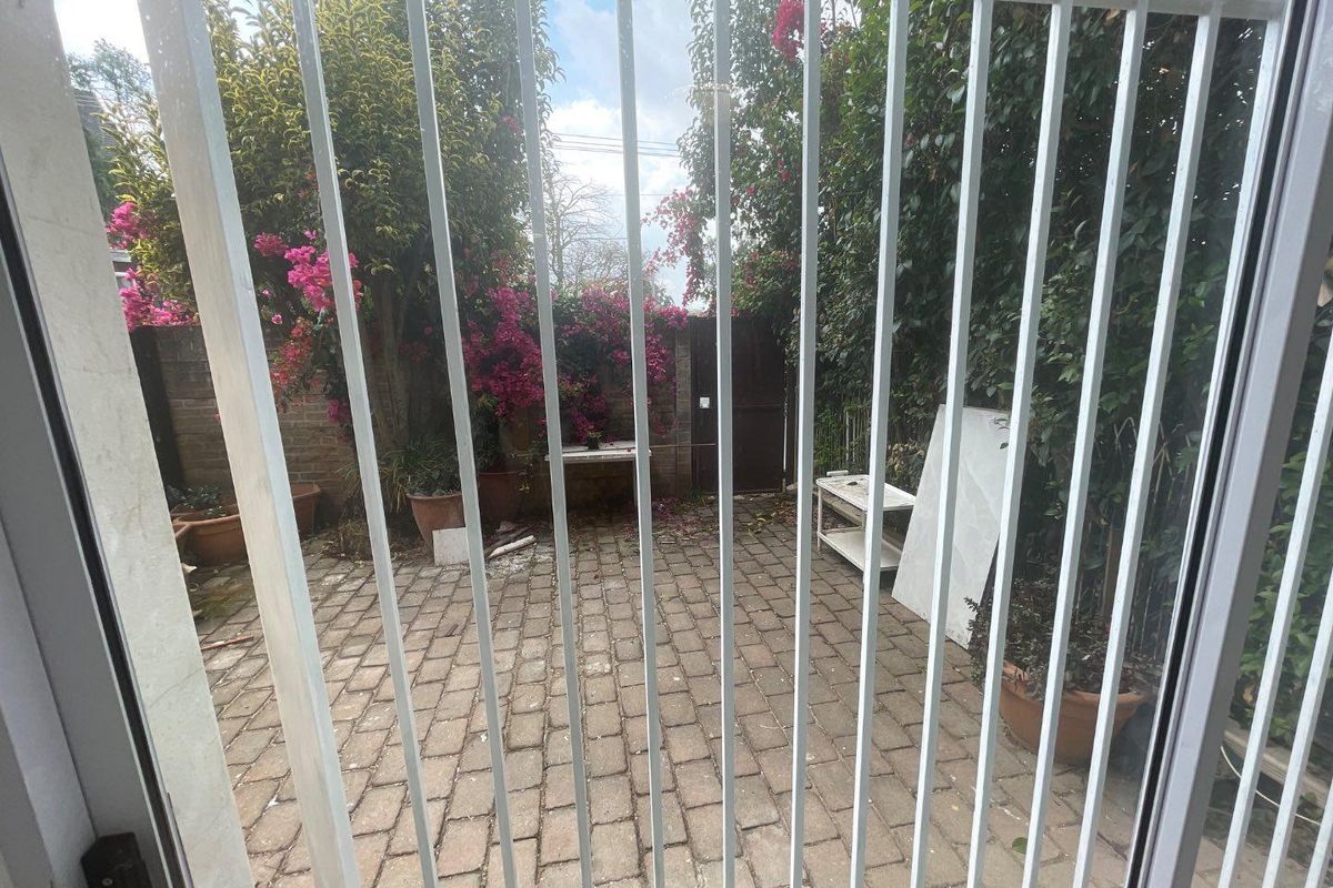 A private rear courtyard featuring brick paving, enclosed by boundary walls and accessed through a secure metal gate.