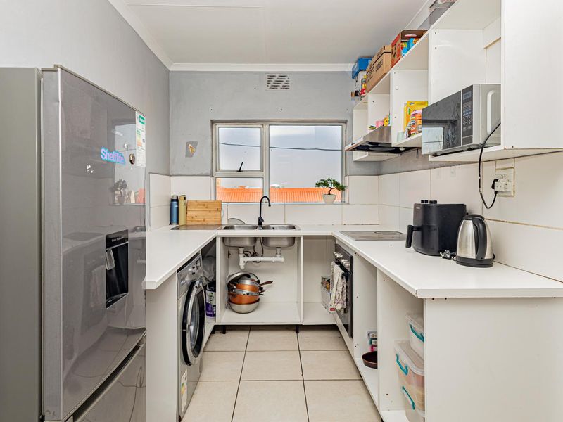 Compact kitchen featuring built-in cabinetry, oven, hob, extractor fan, and integrated laundry plumbing, requiring some cosmetic updates to cabinetry and wall finishes.