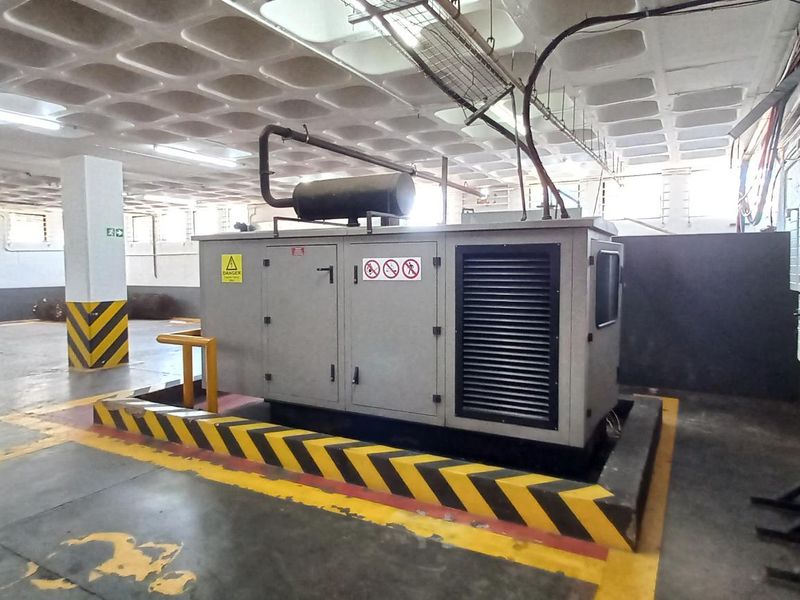 A functional utility space featuring a large backup generator, concrete flooring, and exposed waffle slab ceiling, suitable for industrial or commercial infrastructure support.