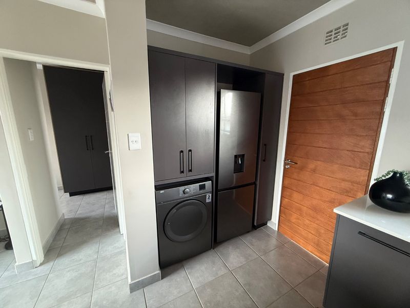 Modern kitchen area featuring dark built-in cabinetry, tiled flooring, and a solid timber door, providing a clean and contemporary aesthetic.