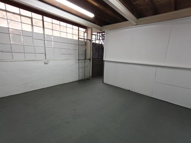 An empty industrial utility space featuring exposed timber beams, large steel-framed windows, and durable painted concrete flooring, suitable for storage or workshop use.