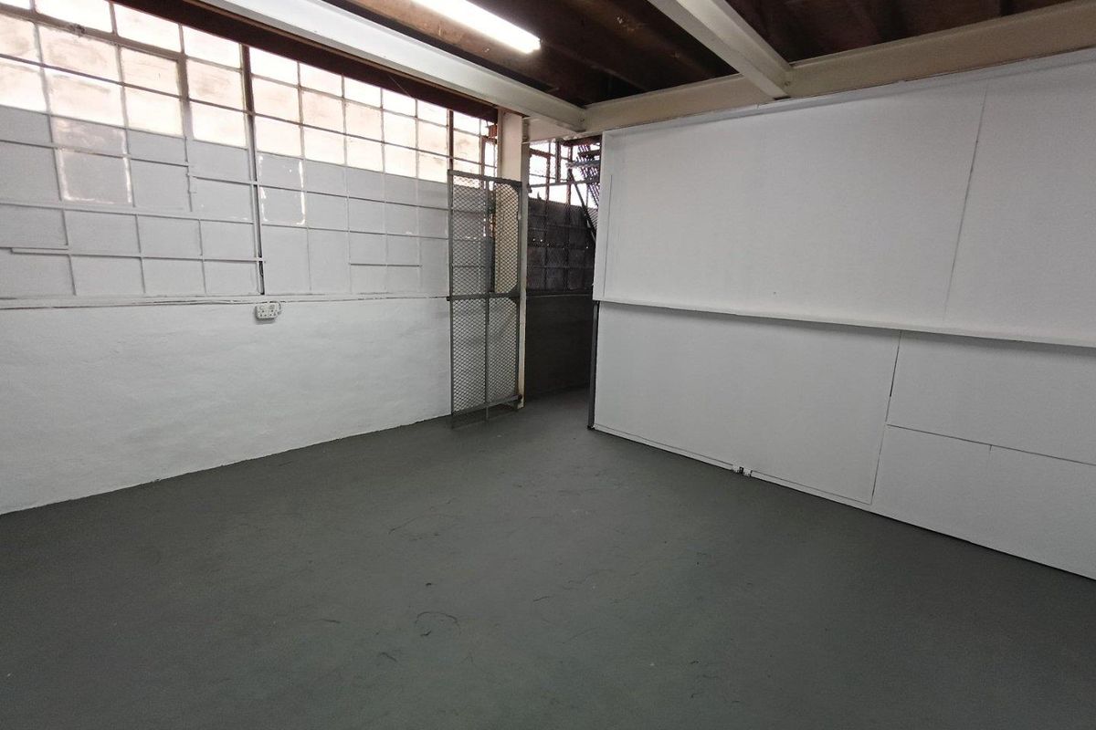 An empty industrial utility space featuring exposed timber beams, large steel-framed windows, and durable painted concrete flooring, suitable for storage or workshop use.