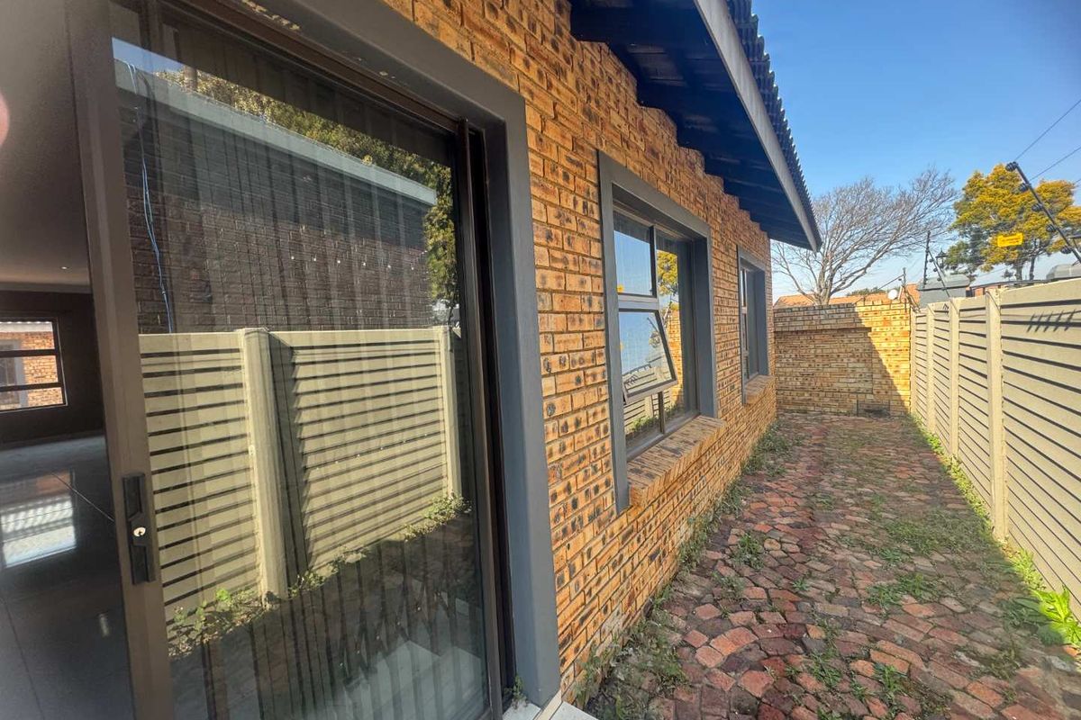 A side exterior view of the cluster home featuring face-brick walls, aluminium window frames, a sliding glass door, and a paved walkway.