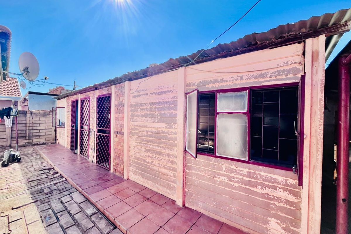 Rear exterior view of the property featuring a paved walkway, brick and plaster wall construction, and metal security gates and window bars.