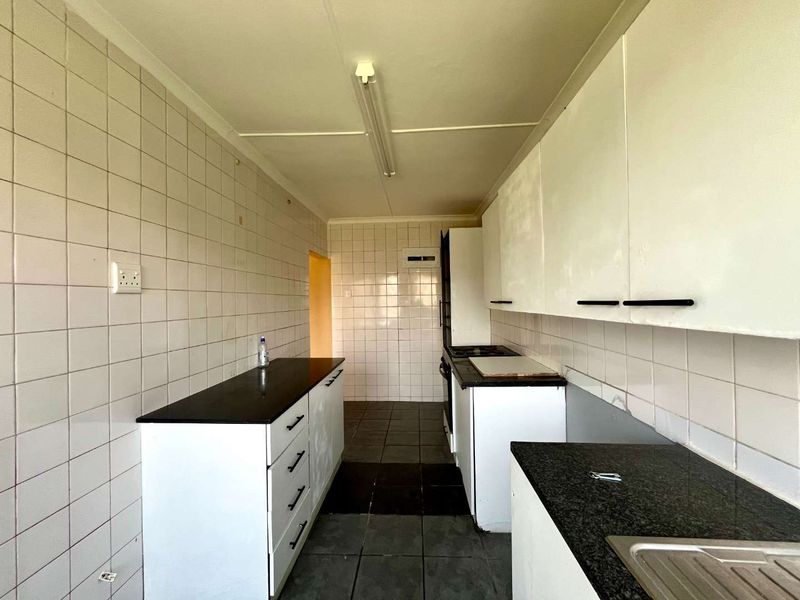 A functional, empty kitchen featuring white built-in cabinetry, dark laminate countertops, tiled splashbacks, and tiled flooring, offering a blank canvas for renovation.