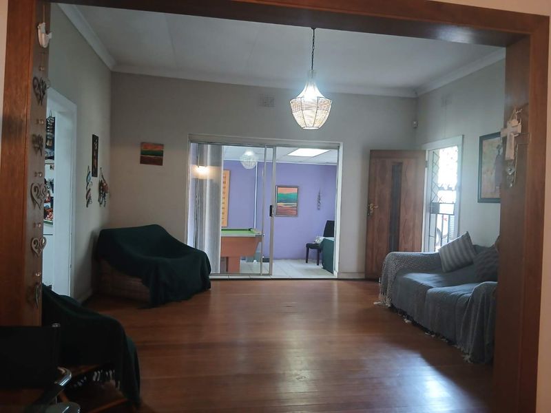 Spacious living room featuring polished hardwood flooring, a central pendant light, and sliding glass doors providing access to an adjacent room.