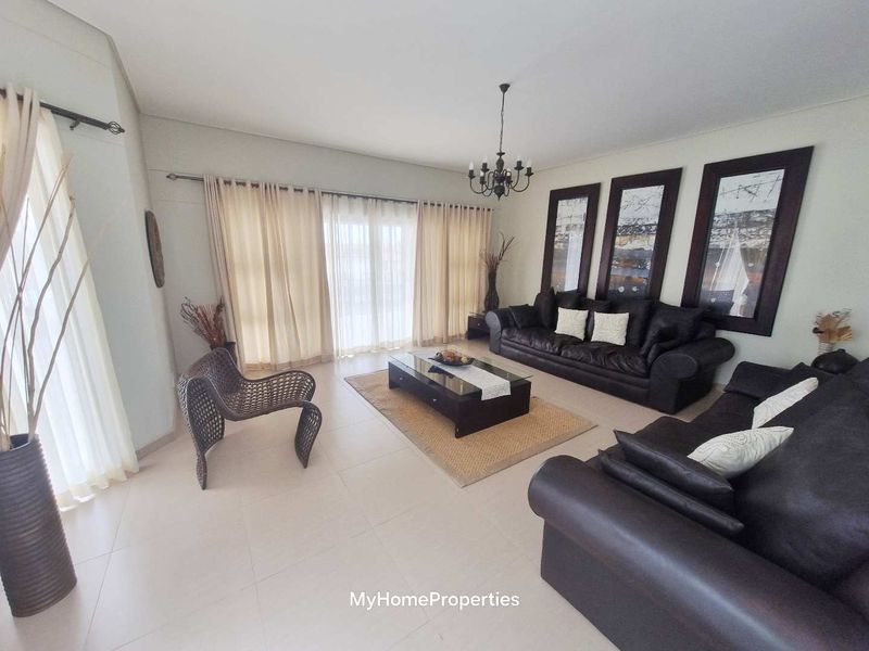 Spacious living room featuring neutral tiled flooring, a central chandelier, and large sliding glass doors providing access to the exterior.