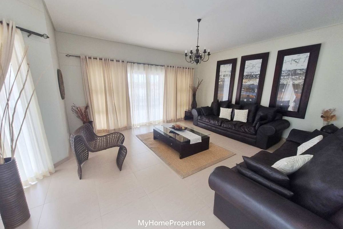 Spacious living room featuring neutral tiled flooring, a central chandelier, and large sliding glass doors providing access to the exterior.