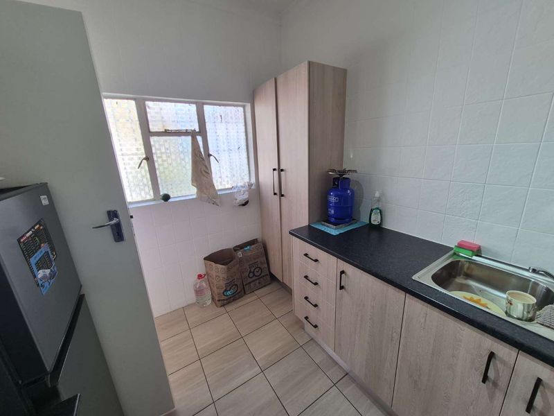 A functional scullery area featuring built-in cabinetry, laminate countertops, a stainless steel sink, and tiled splashbacks.