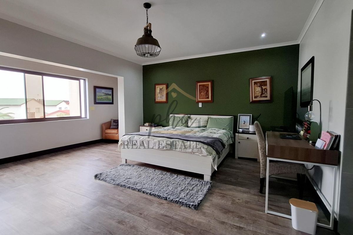 Spacious bedroom featuring modern laminate flooring, a feature wall, and large sliding windows that provide ample natural light.