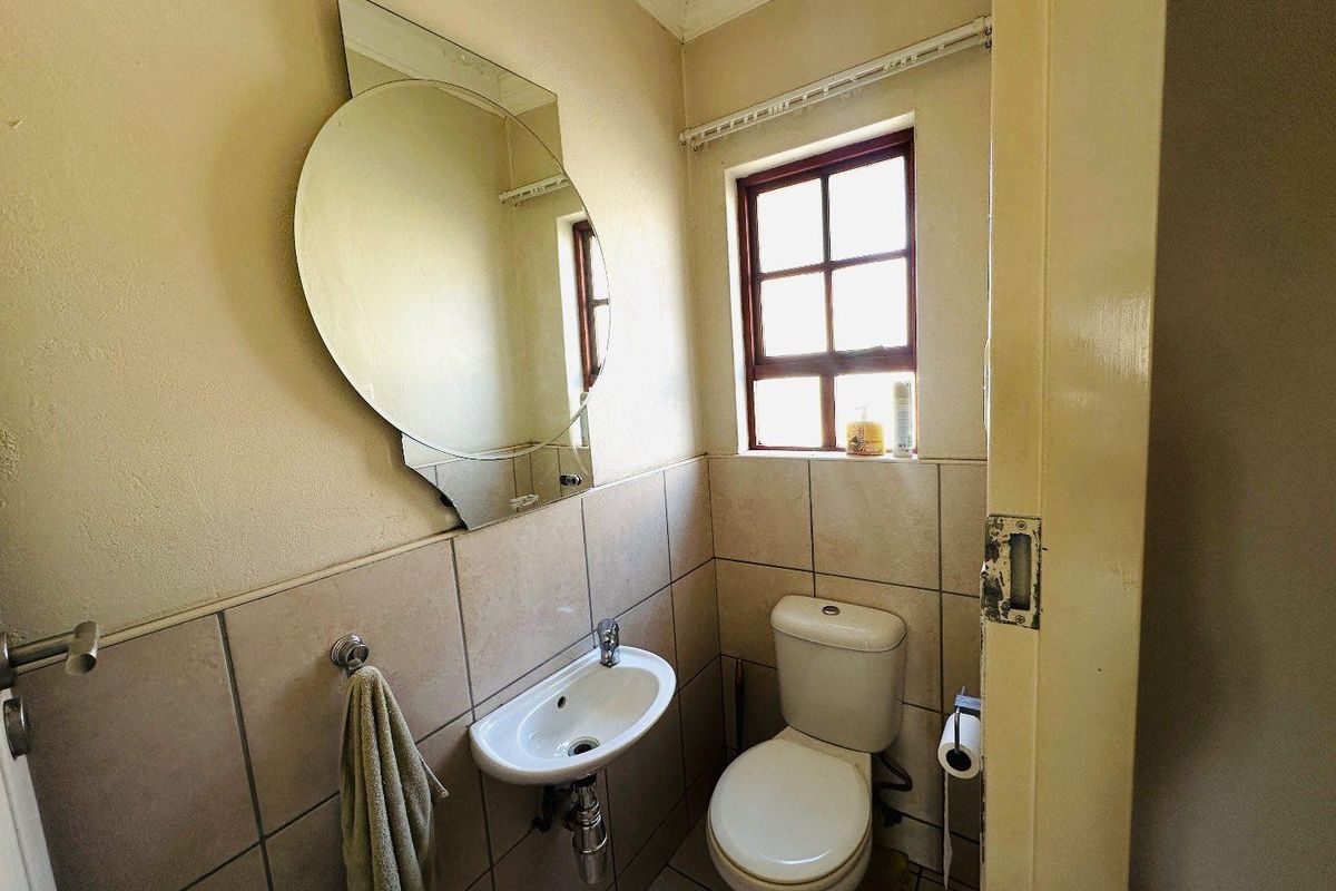 A compact guest bathroom featuring a wall-mounted basin, toilet, and tiled finishes, requiring cosmetic updates to modernize the space.
