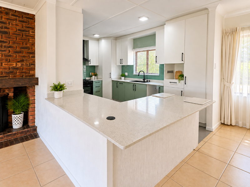 Modern kitchen featuring quartz countertops, sage green and white cabinetry, subway tile backsplash, and an adjacent brick fireplace, creating a warm, functional space.