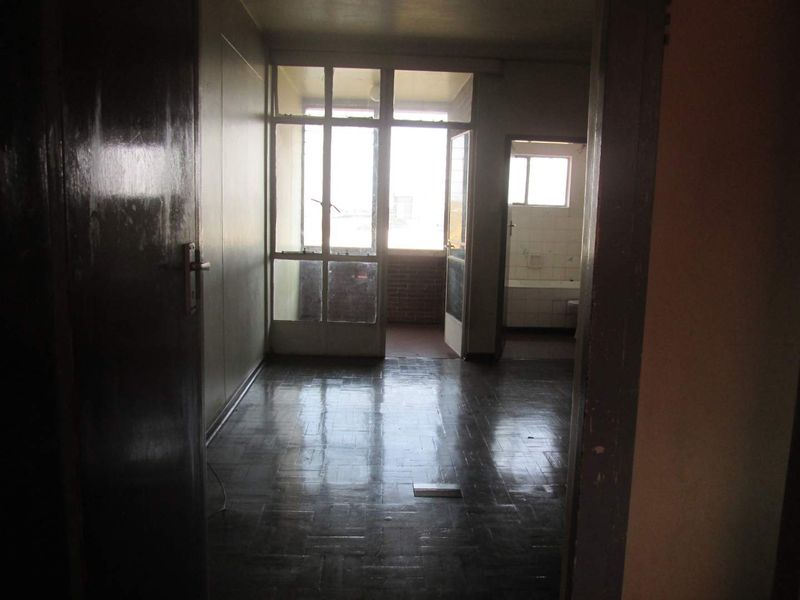 An empty living area featuring dark parquet flooring, leading to a balcony and an adjacent bathroom with dated finishes.