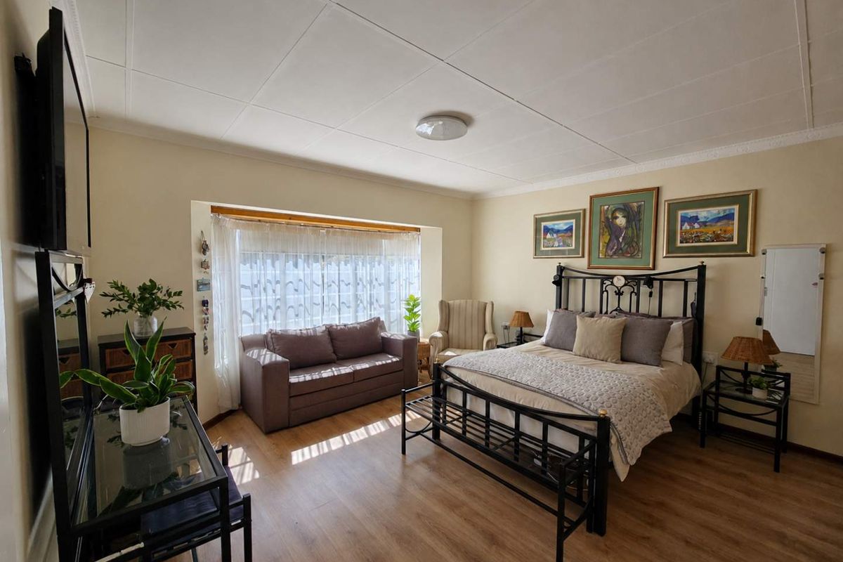 Spacious bedroom featuring laminate flooring, a large bay window providing natural light, and a classic tiled ceiling finish.