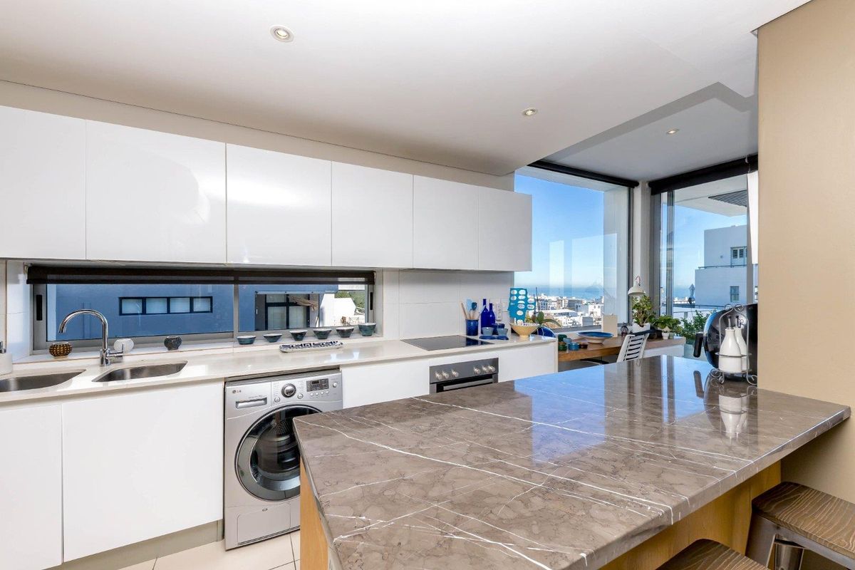 Modern kitchen featuring sleek white gloss cabinetry, stone countertops, built-in appliances, and expansive windows offering panoramic coastal views.