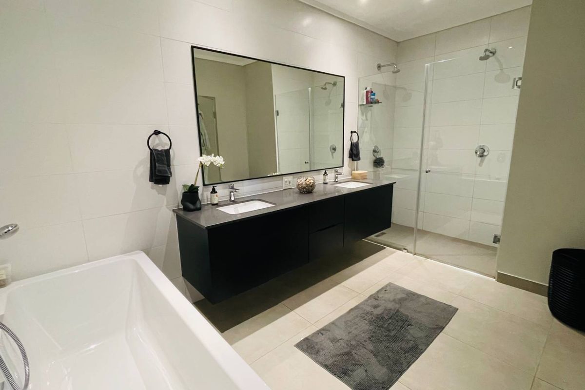 Modern bathroom featuring a floating double vanity, large frameless glass shower, and a deep soaking bathtub with contemporary fixtures and neutral tiling.