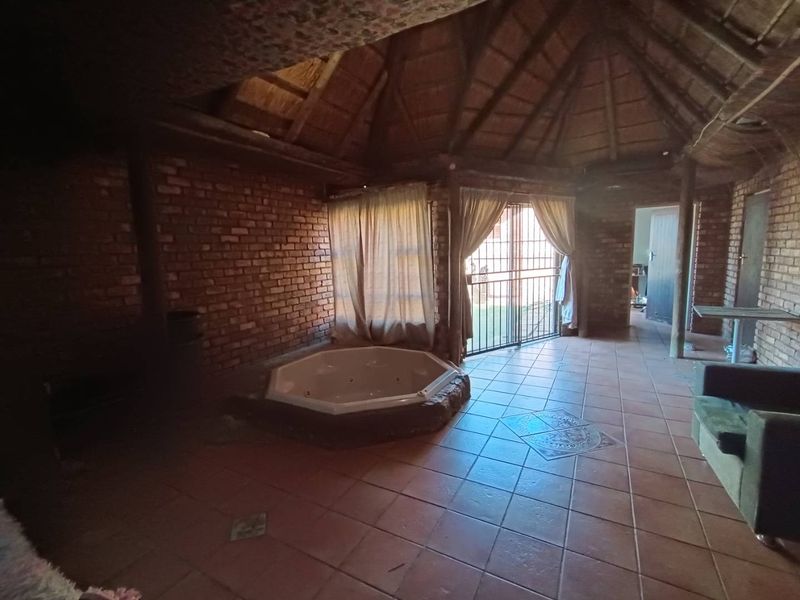 Spacious living area featuring a built-in jacuzzi, exposed brick walls, and a traditional thatched roof, offering a unique rustic aesthetic.