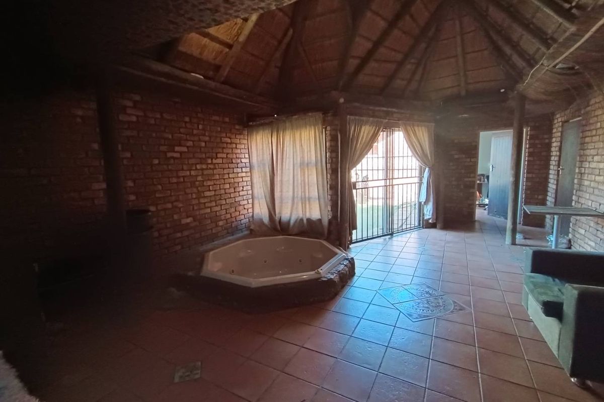 Spacious living area featuring a built-in jacuzzi, exposed brick walls, and a traditional thatched roof, offering a unique rustic aesthetic.