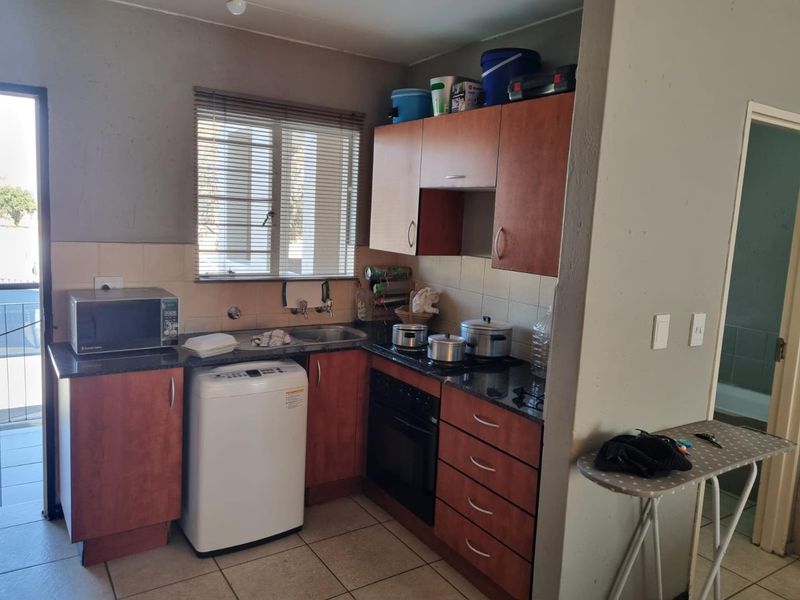 Compact kitchen featuring wooden cabinetry, granite countertops, built-in oven and hob, and tiled flooring with direct access to an outdoor area.
