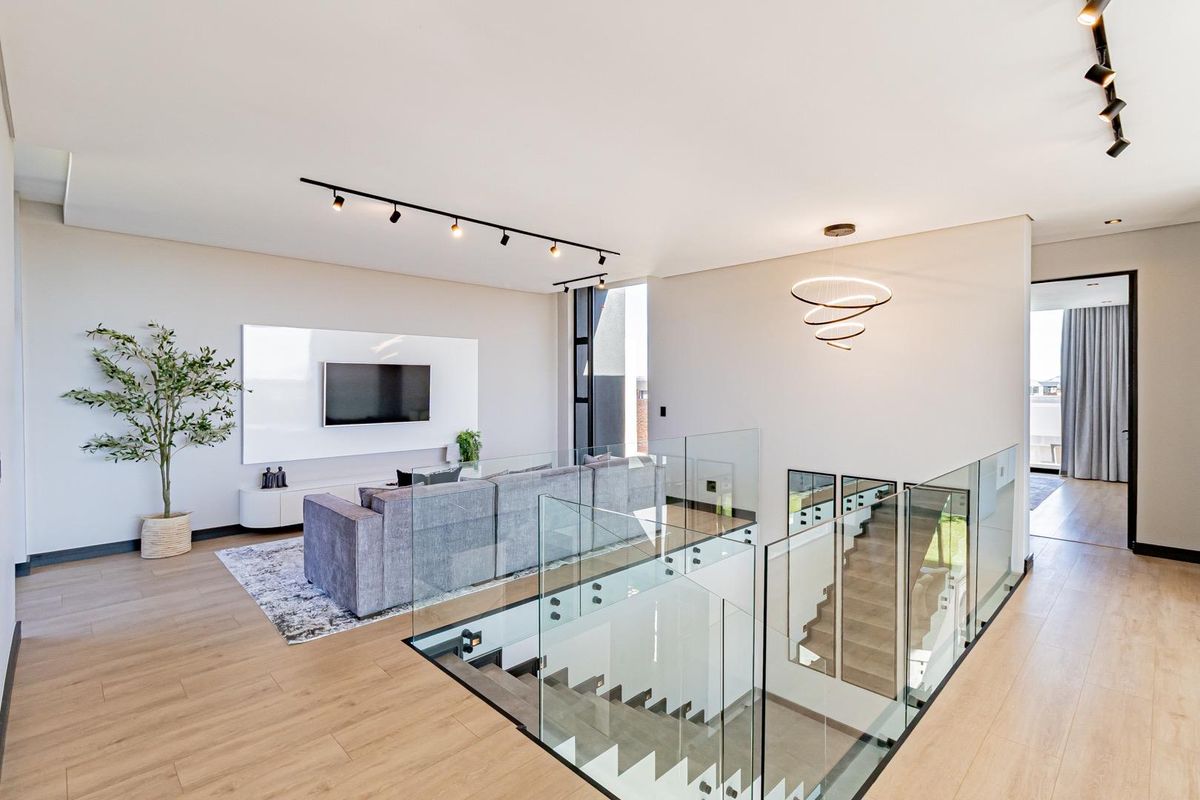 Modern open-plan living area featuring light wood-look flooring, contemporary track lighting, and a sleek glass balustrade overlooking the staircase.