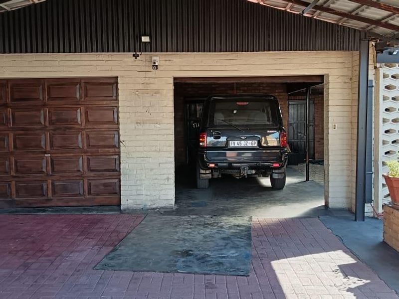 A functional garage area featuring a sectional door, brick construction, and paved driveway space under a corrugated metal roof structure.