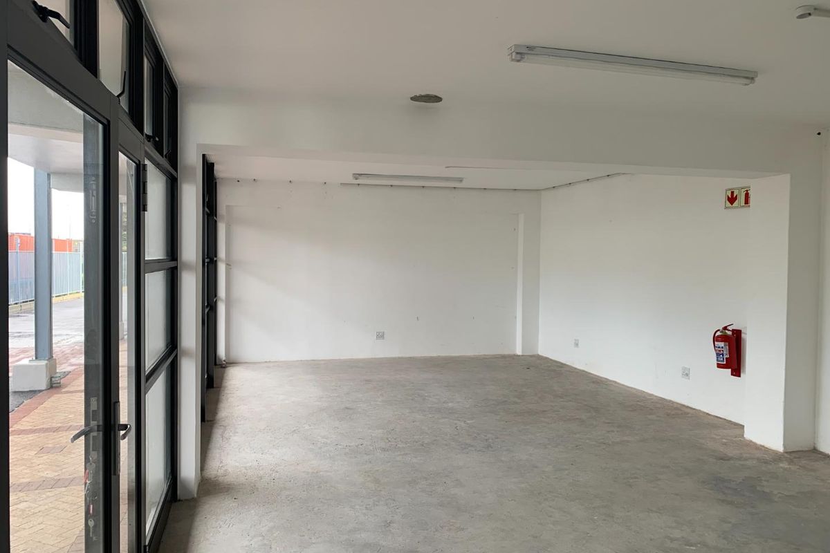 An empty, open-plan commercial space featuring black aluminium-framed glass doors, concrete flooring, and functional strip lighting, suitable for various business uses.